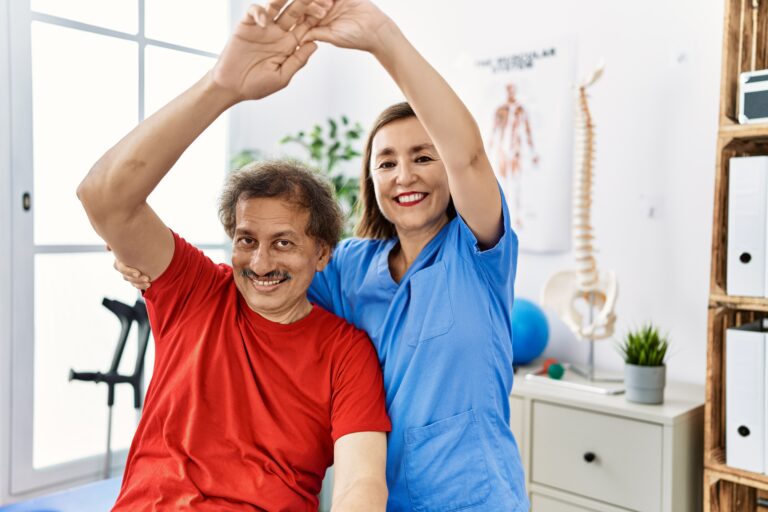Middle age man and woman wearing physiotherapy uniform having rehab session stretching arm at physiotherapy clinic